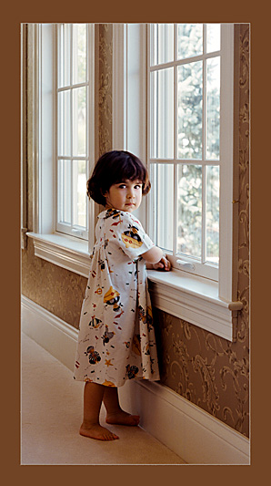 A young girl standing by a window looking back over her shoulder